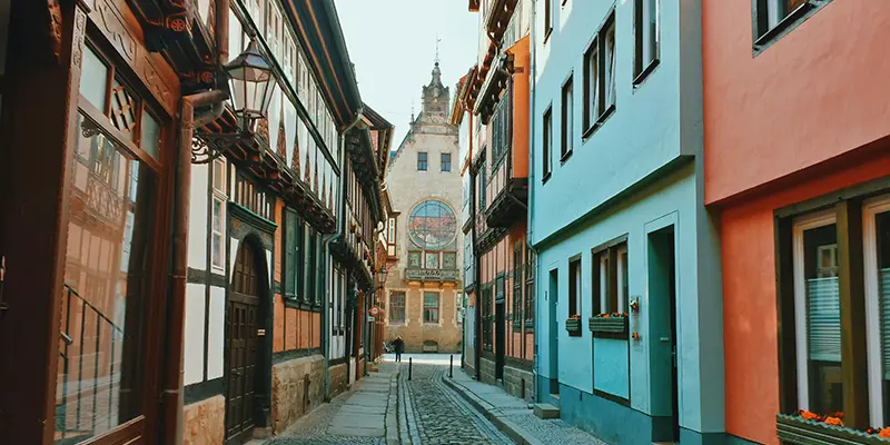 A curving cobbled pedestrian street lined with colourful houses and a tower at the end